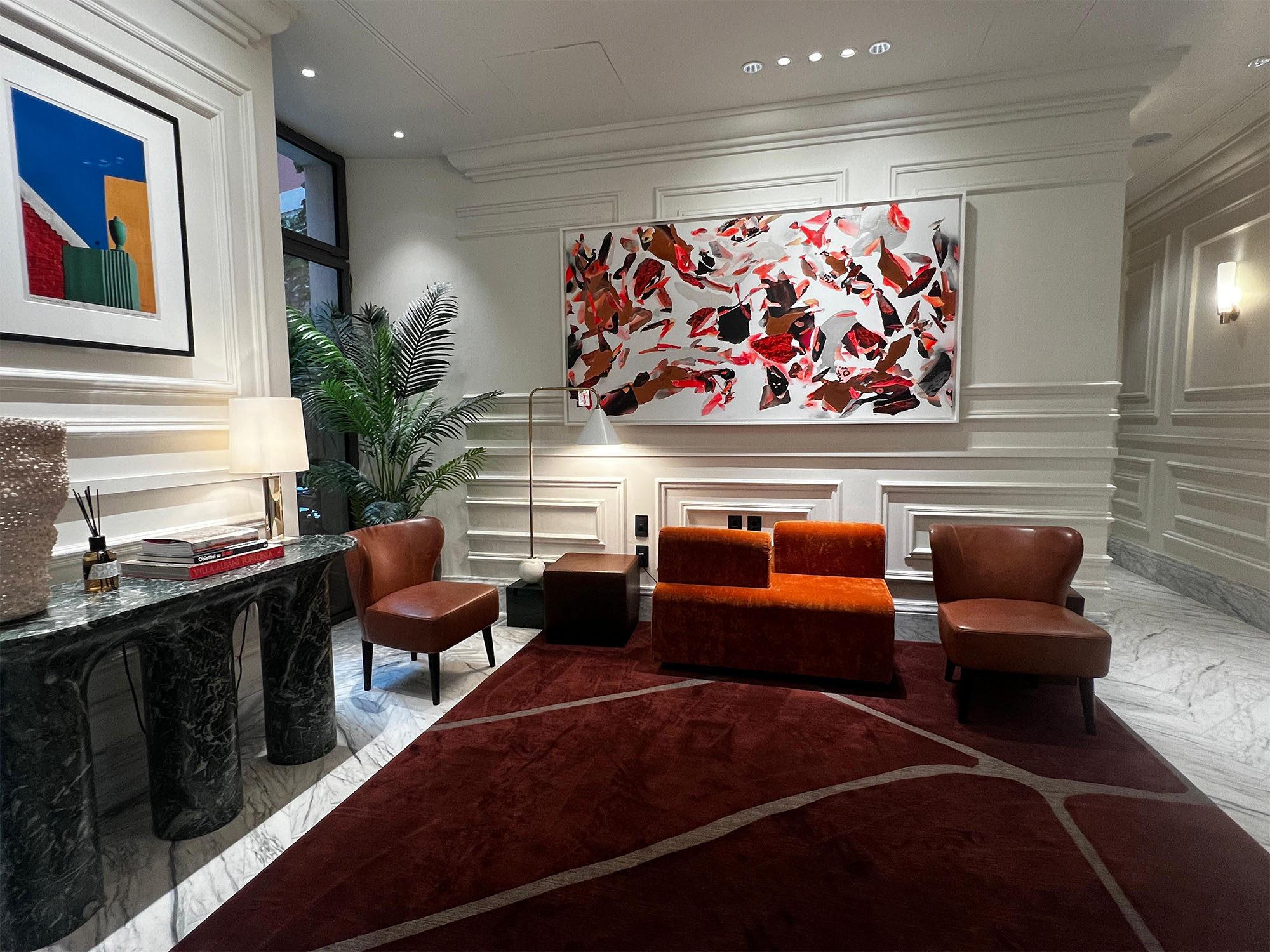 Elegant hotel lounge with an abstract red painting, rust-coloured armchairs and a dark marble console