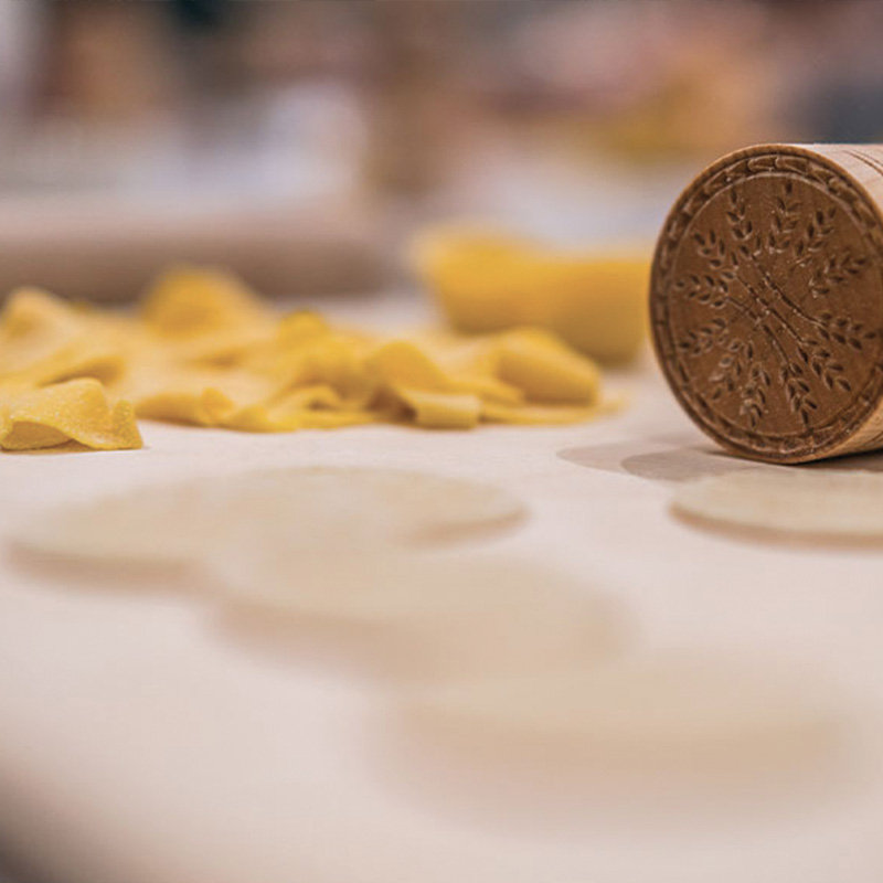 Fresh egg pasta and a carved wooden pasta stamp on a floured work surface