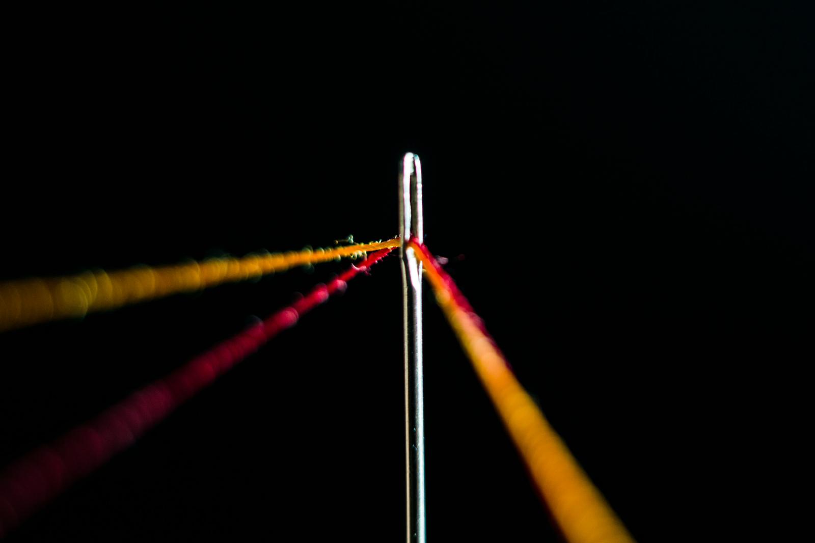 Close-up of a needle threaded with red and orange thread against a black background