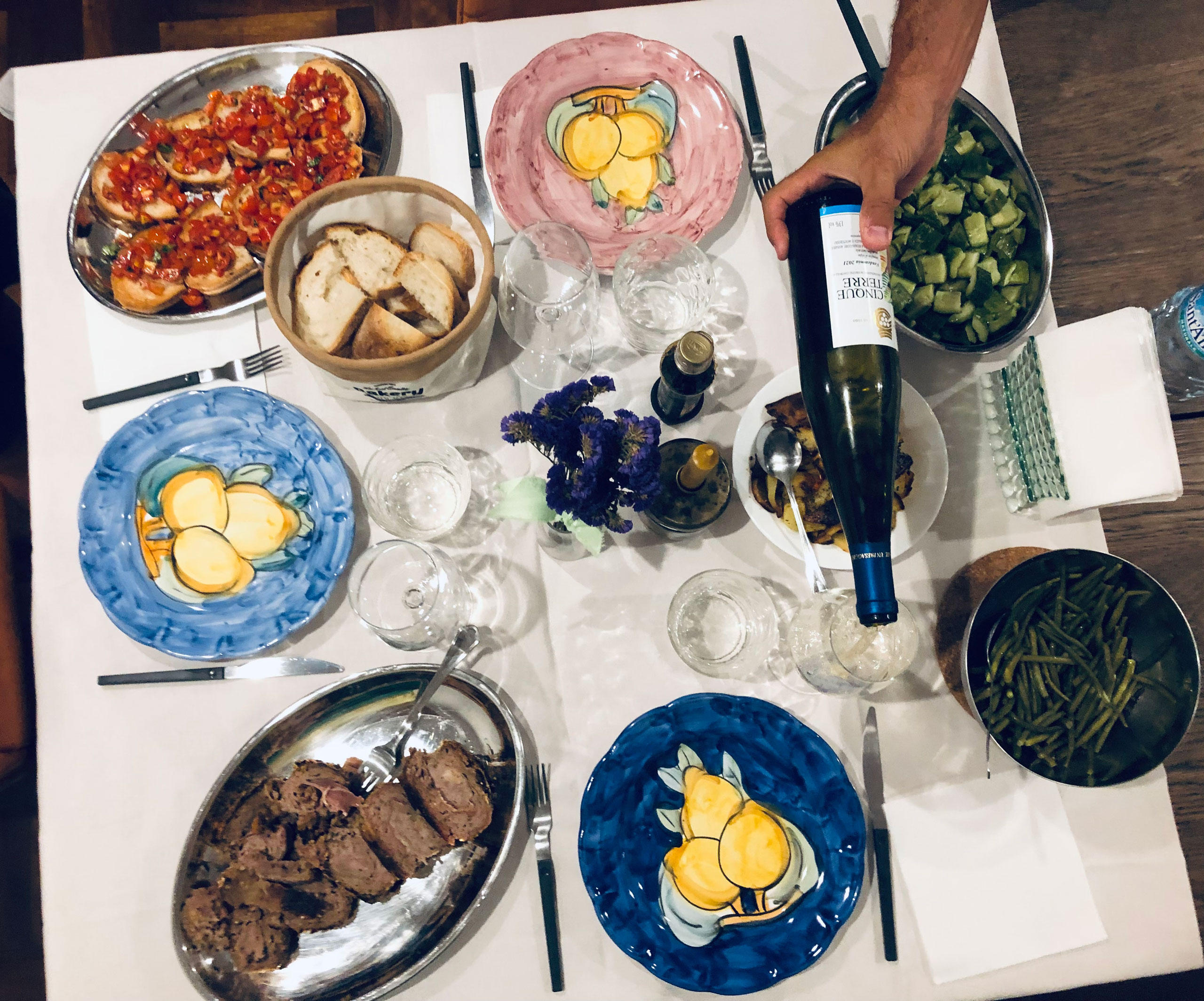 Overhead view of a family-style table with antipasti, roast meat, vegetables and a bottle of wine being poured