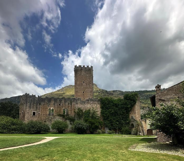 Medieval stone castle with a square tower rising above a green lawn under a dramatic cloudy sky
