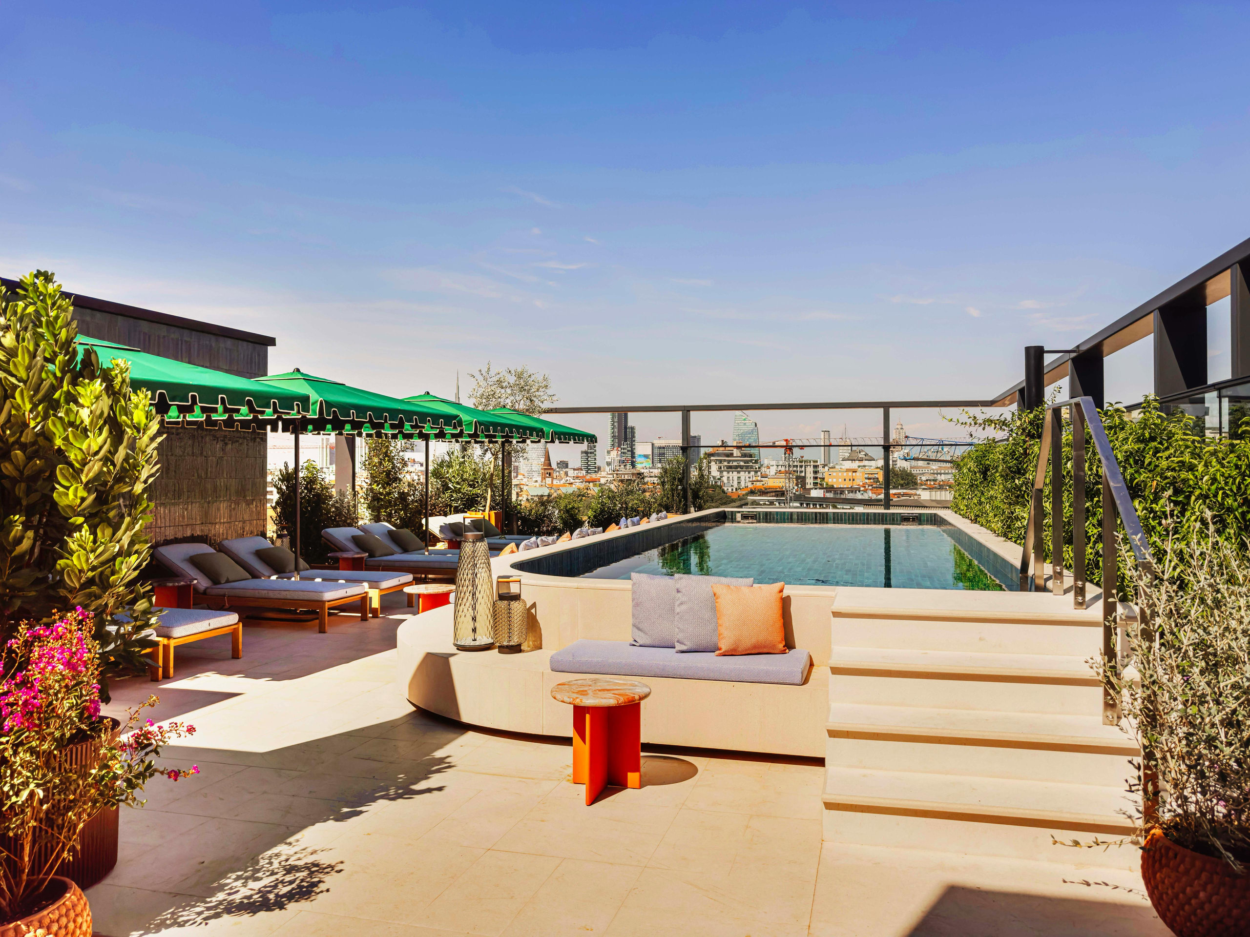 Hotel rooftop terrace with a pool, green parasols and sun loungers overlooking the city skyline