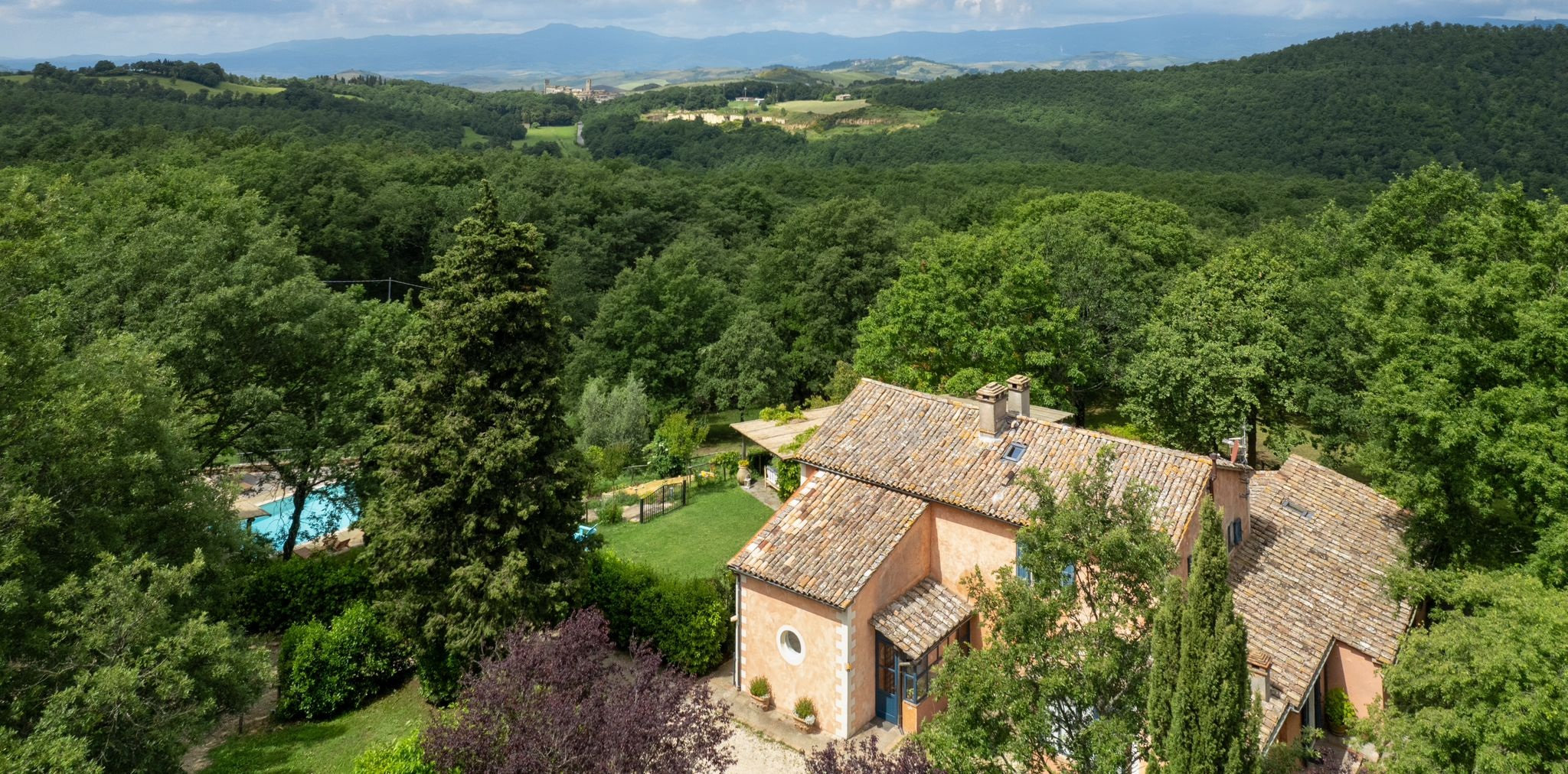 Aerial view of a terracotta-roofed villa with a pool, surrounded by dense green woodland