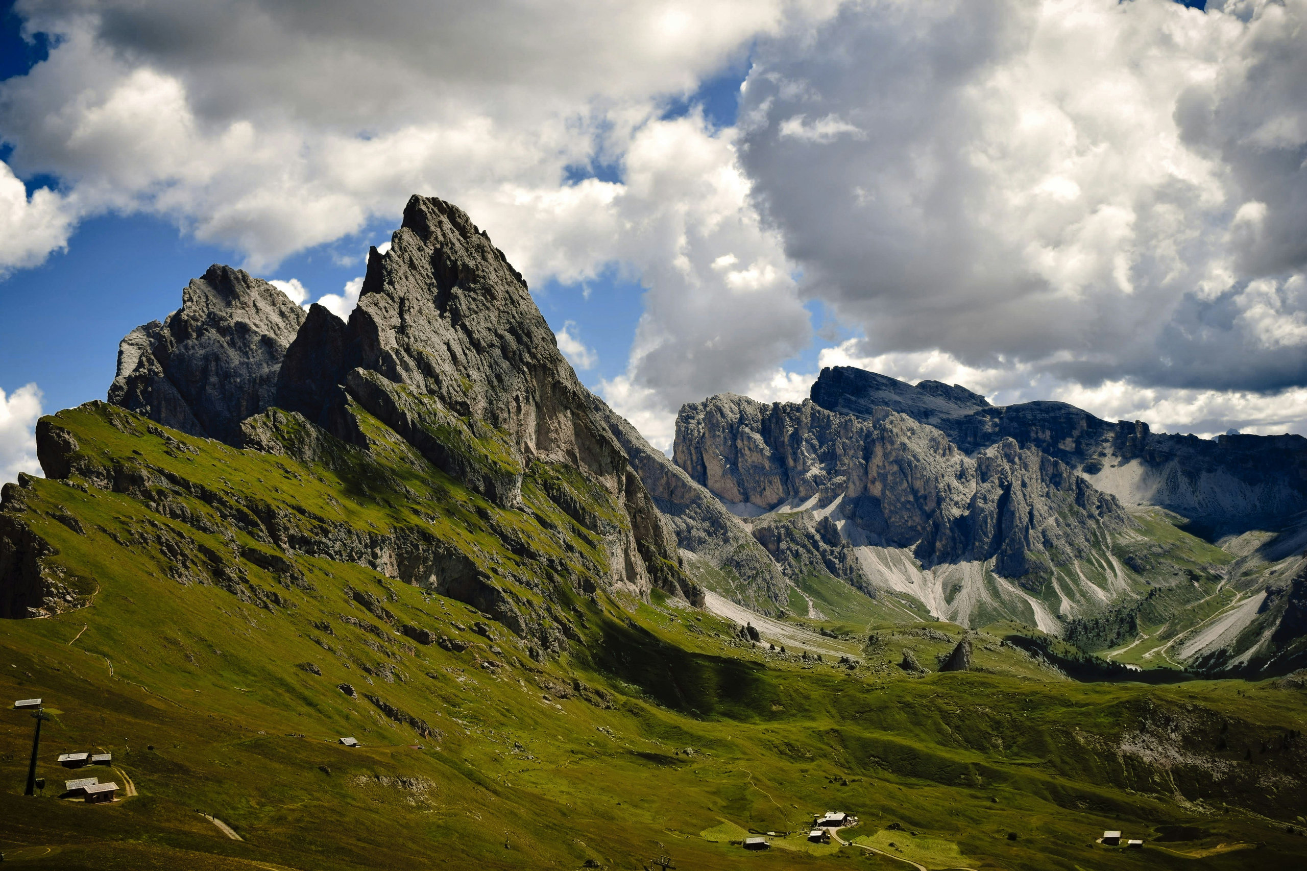 Jagged Dolomite peaks above green alpine meadows under a sky of billowing clouds