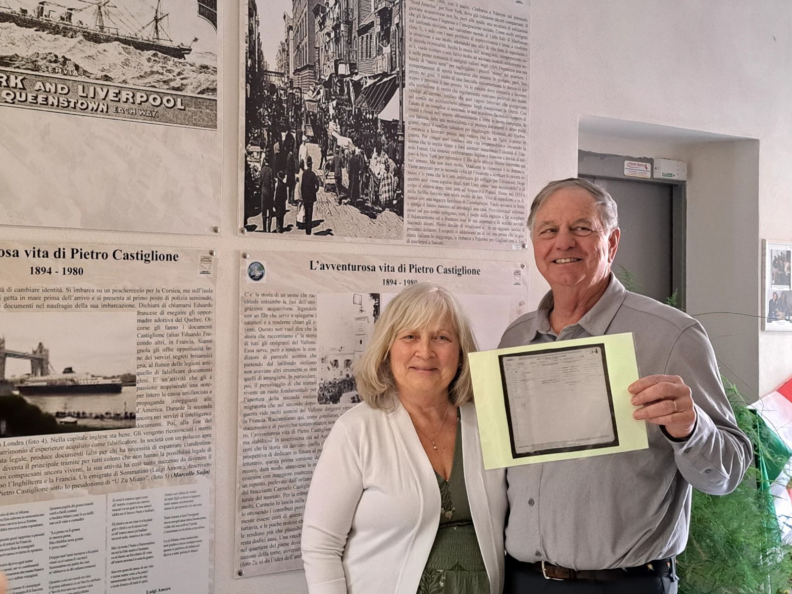 Two travellers holding a framed document in front of a village archive display