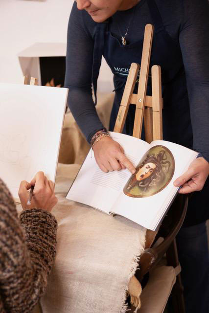 Hands holding an open book beside an easel in an artisan's workshop