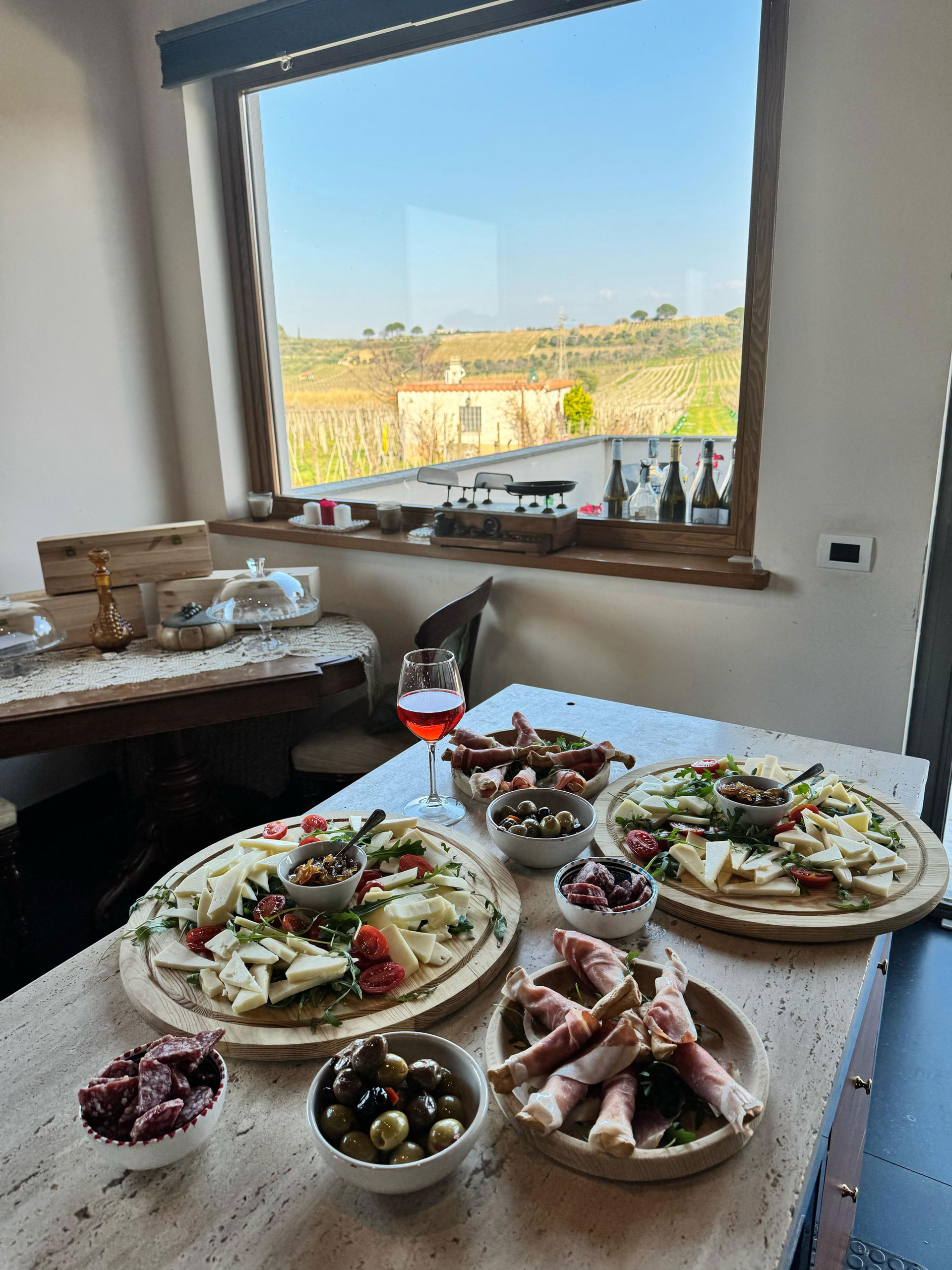 A table of Roman cured meats, cheese, olives and wine in front of a window over the countryside