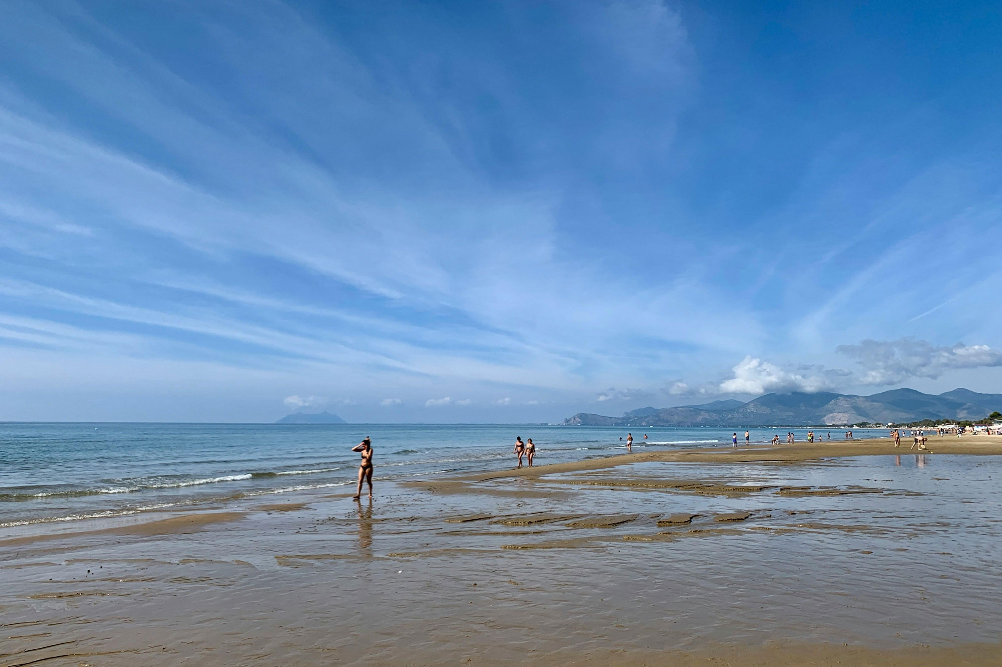 A wide sandy beach near Rome with bathers at the water's edge