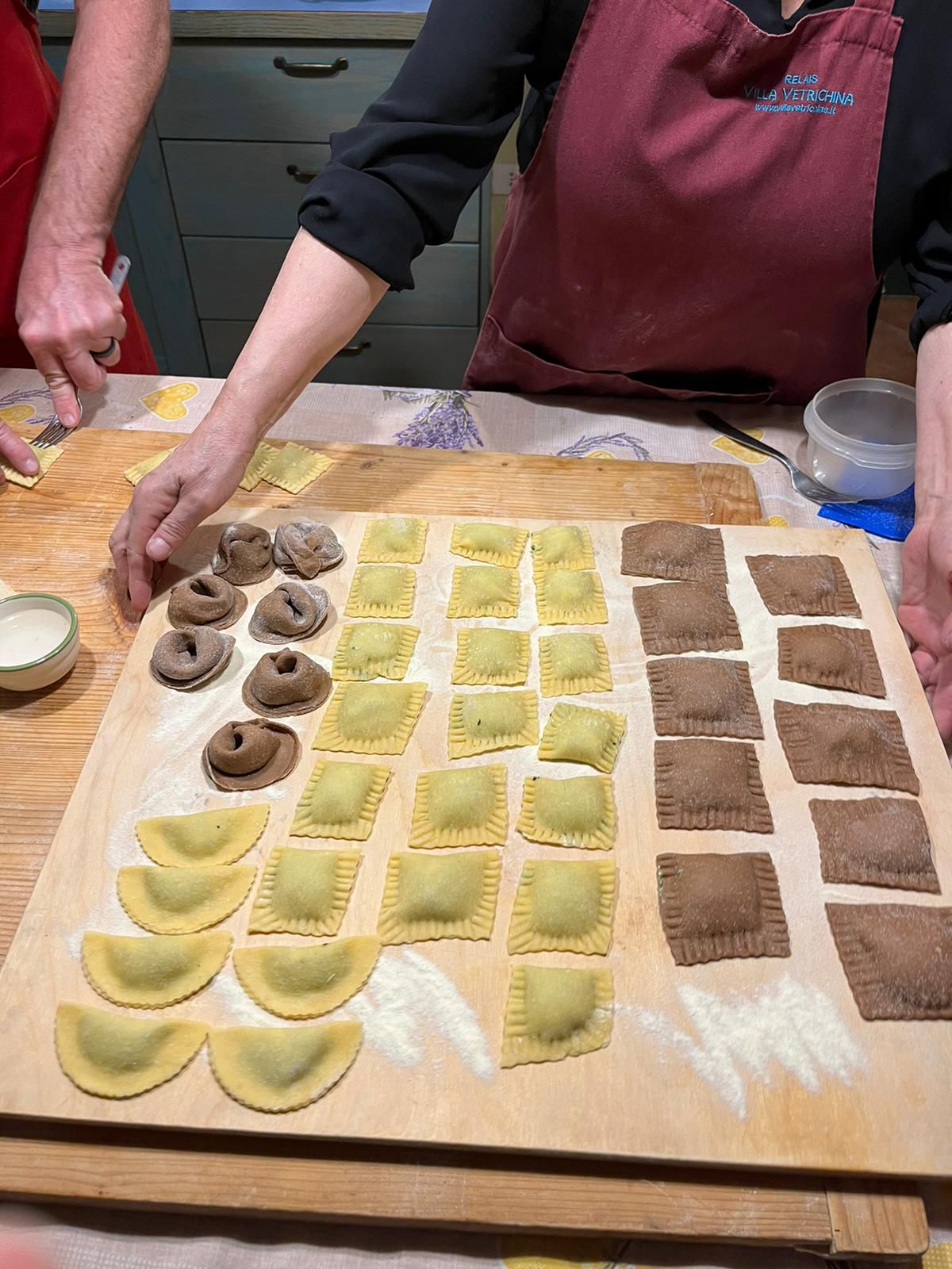 Hands shaping filled pasta on a wooden board during a cookery class