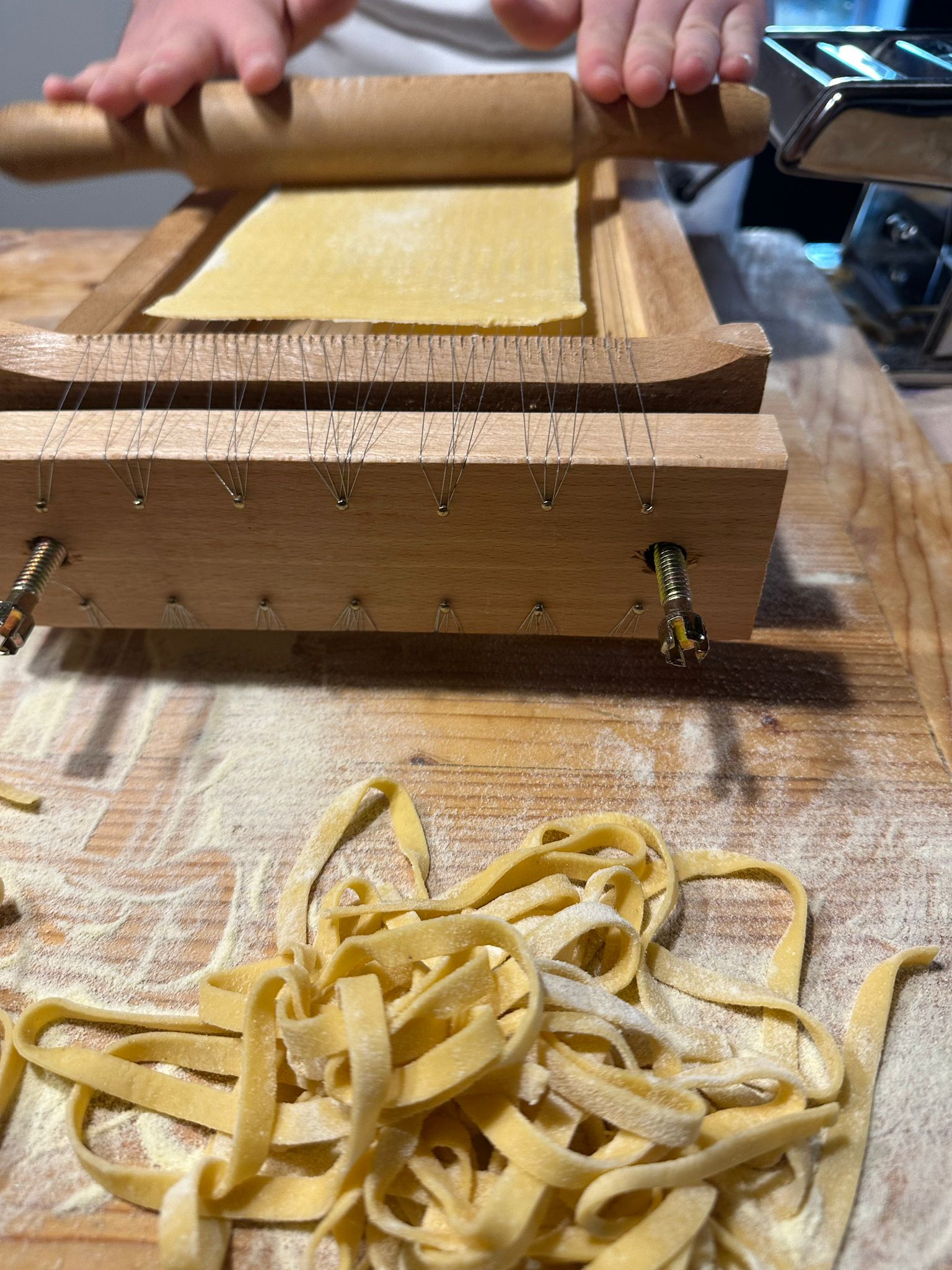 Fresh tagliatelle beside a hand-cranked pasta cutter