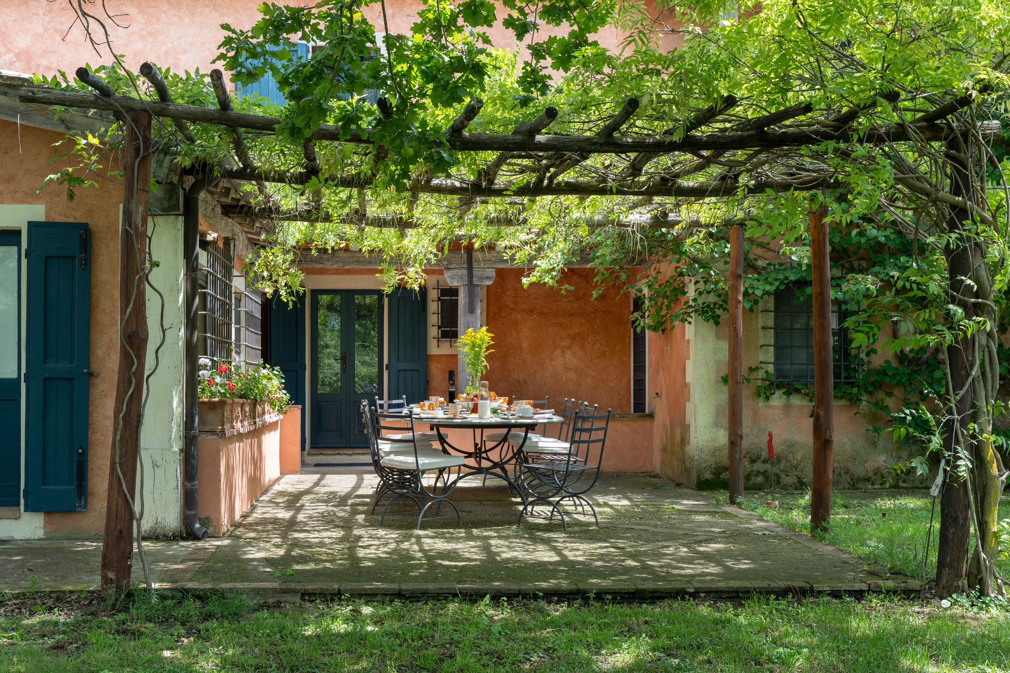 A shaded pergola with a long table in the villa's garden