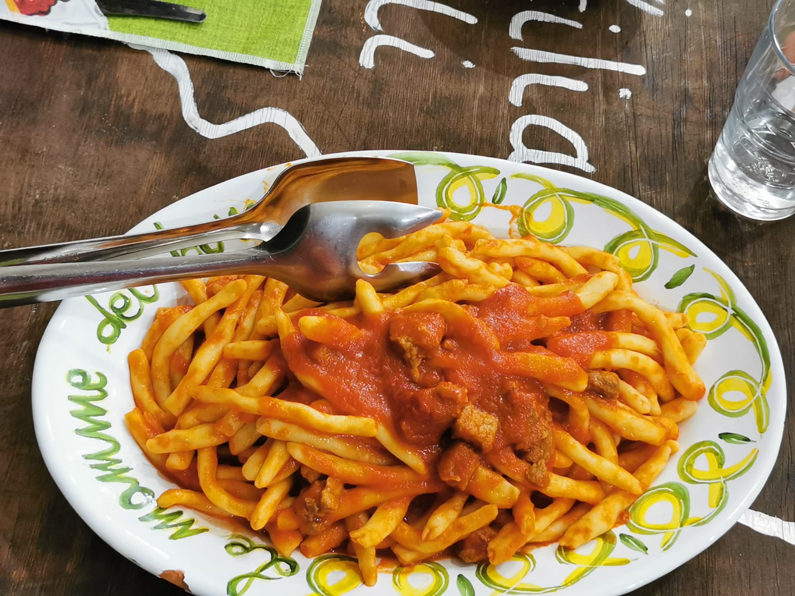 Plate of short pasta in tomato and sausage sauce on a rustic table with serving tongs
