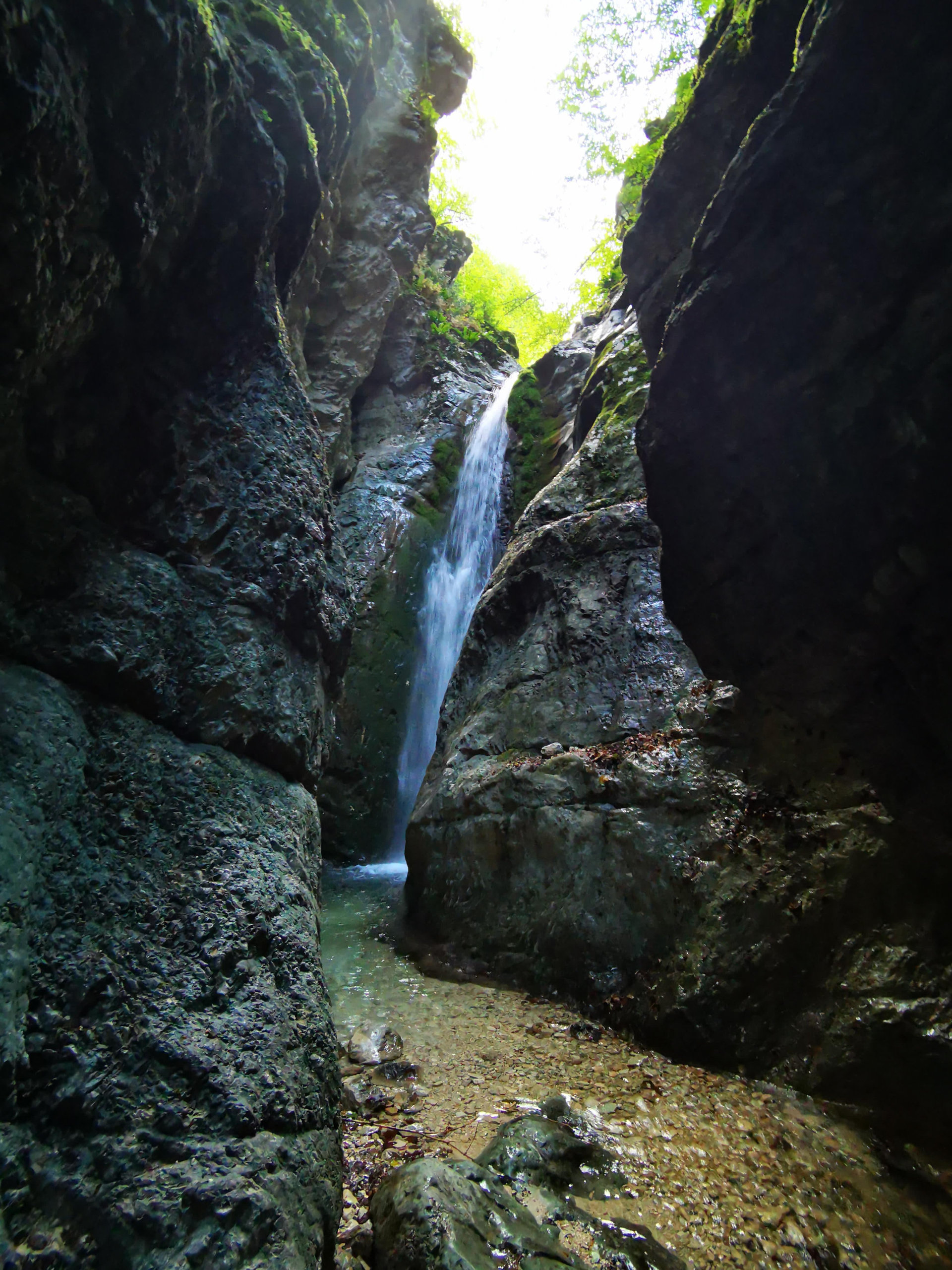 A waterfall dropping into a narrow green gorge in the Lacerno canyon
