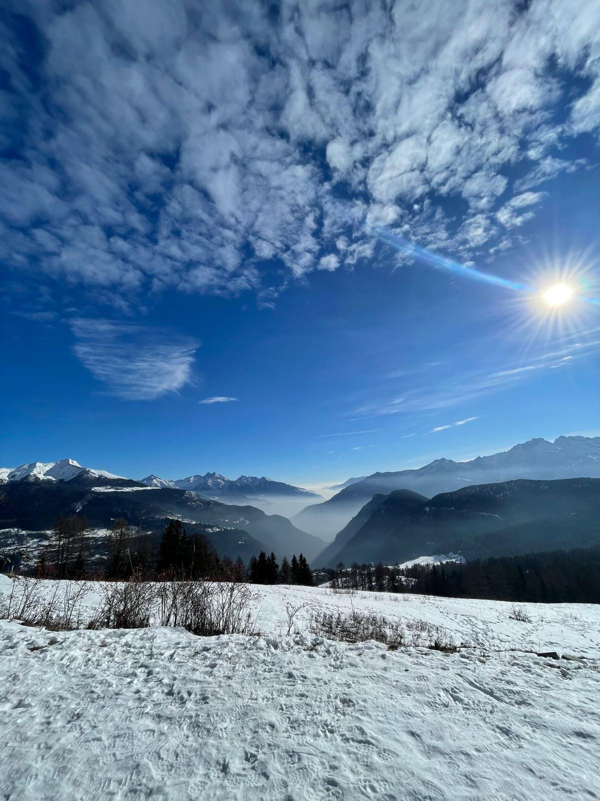 Snow-covered hills under a low winter sun, mountains on the horizon