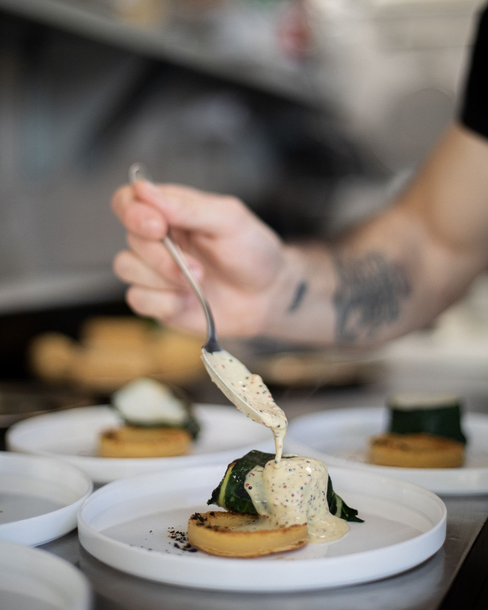 A chef spooning sauce onto a plated dish