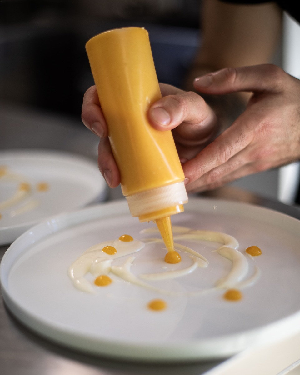 A chef drawing a spiral of sauce onto a plate