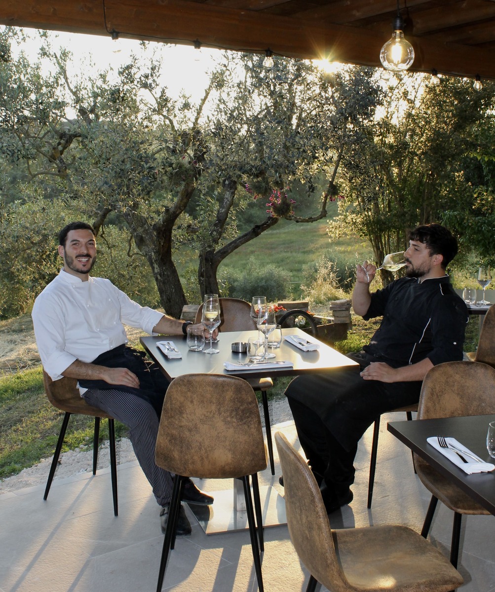 Two guests eating at a table under olive trees at dusk