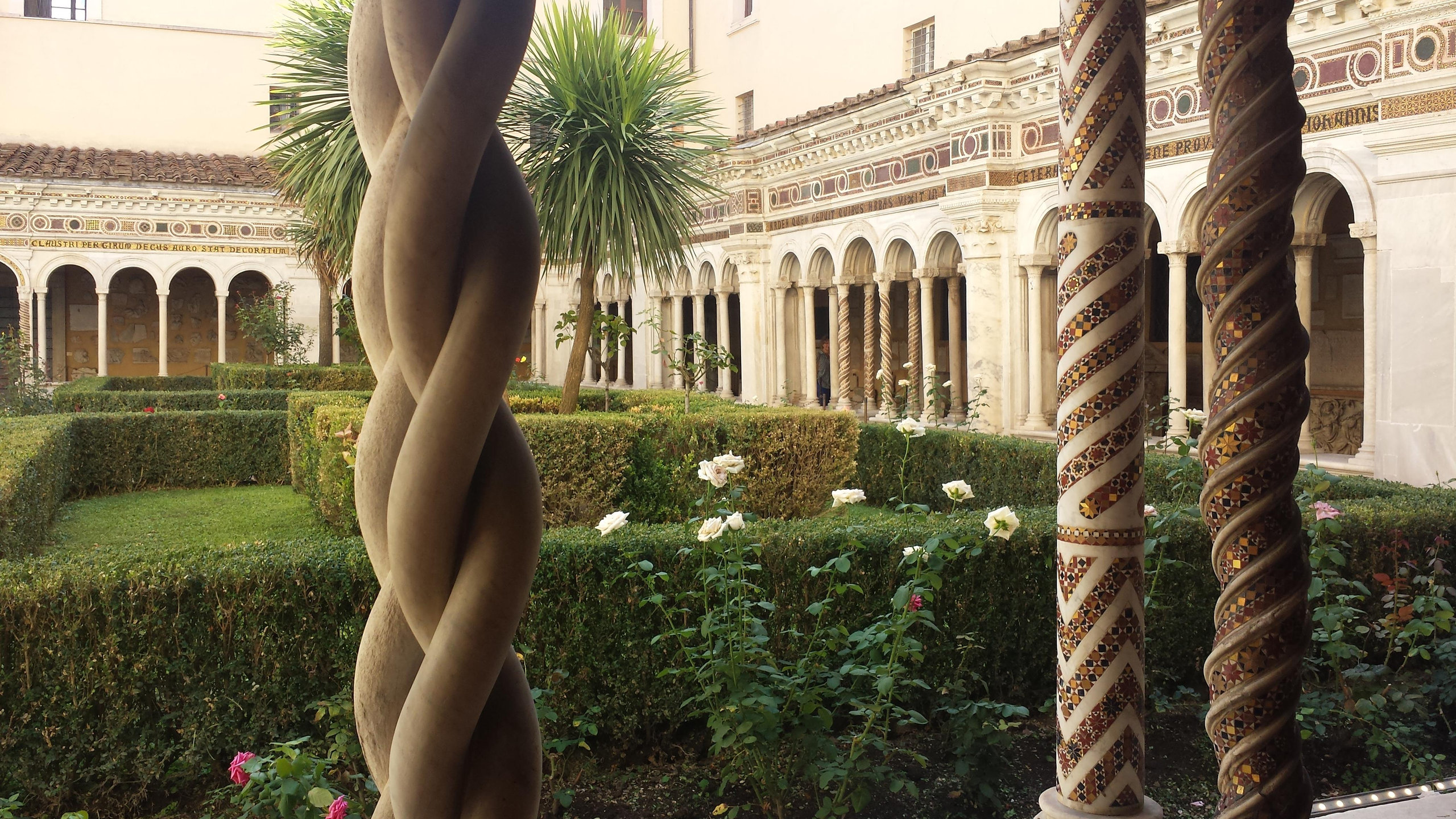 Cloister garden with roses and clipped hedges framed by twisted mosaic-inlaid columns