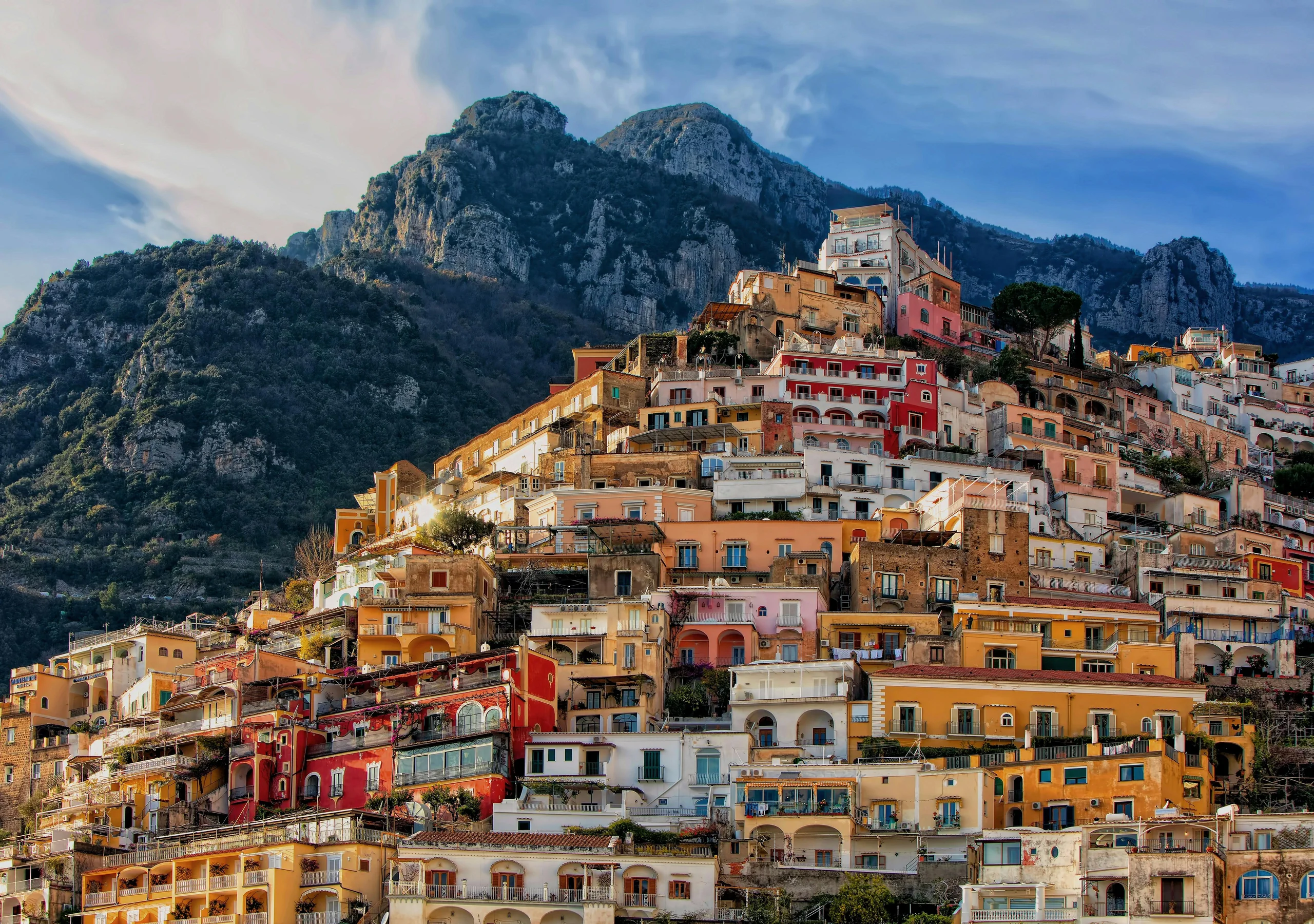 Pastel-coloured houses stacked up a steep hillside with rugged mountains behind, on the Amalfi Coast
