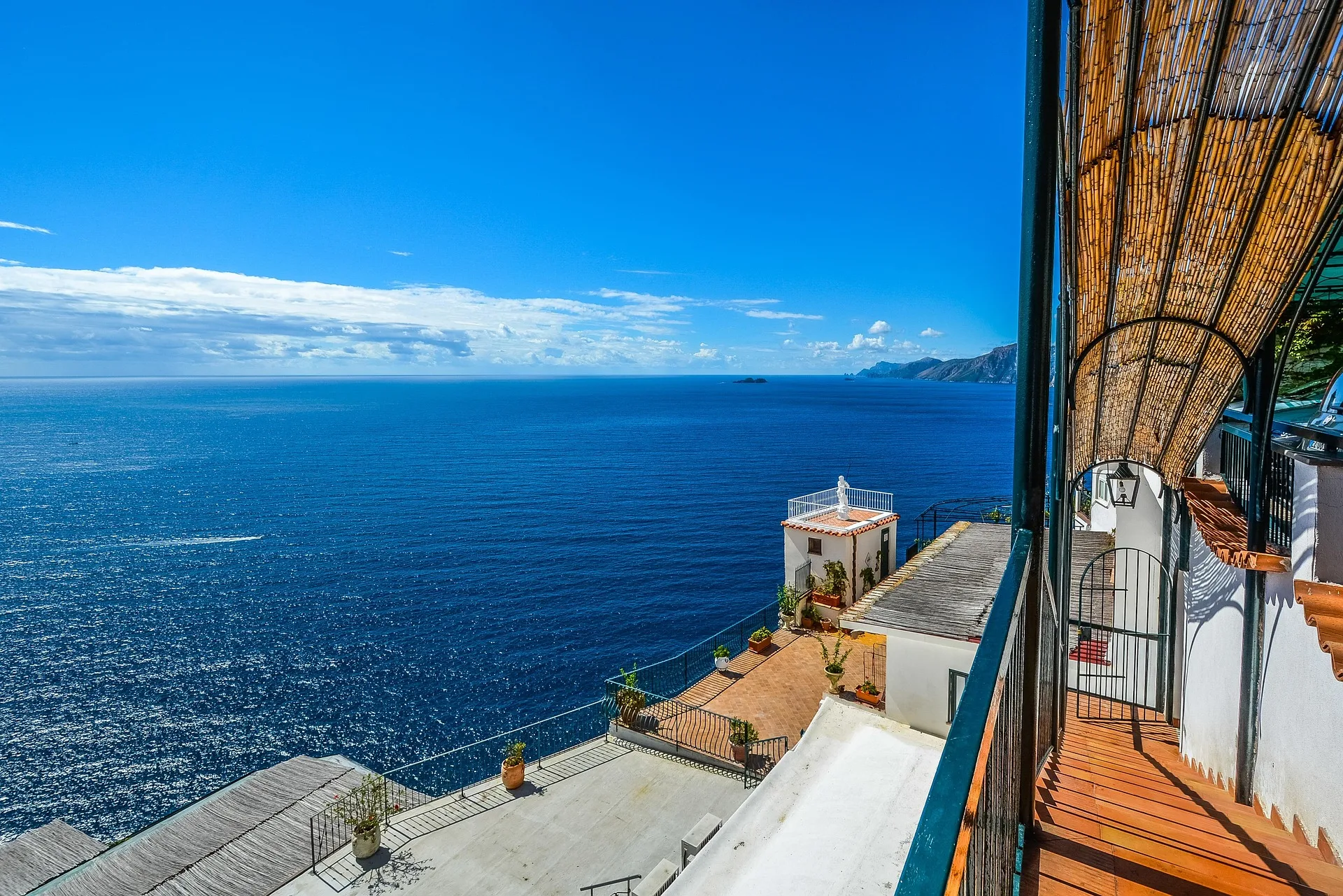 Seaside terrace with a bamboo-roofed balcony looking over the deep blue Mediterranean and a small chapel