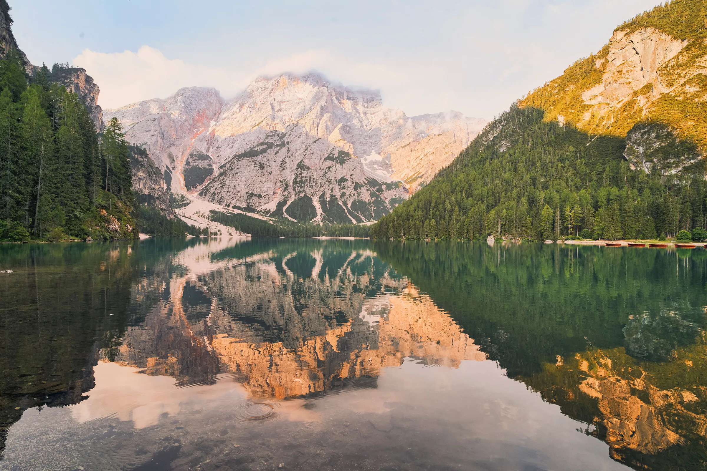 Alpine lake mirroring pale rocky peaks and a forested slope at golden light