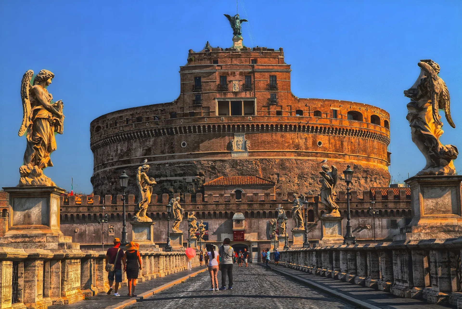 Castel Sant'Angelo seen from the bridge lined with angel statues under a deep blue sky