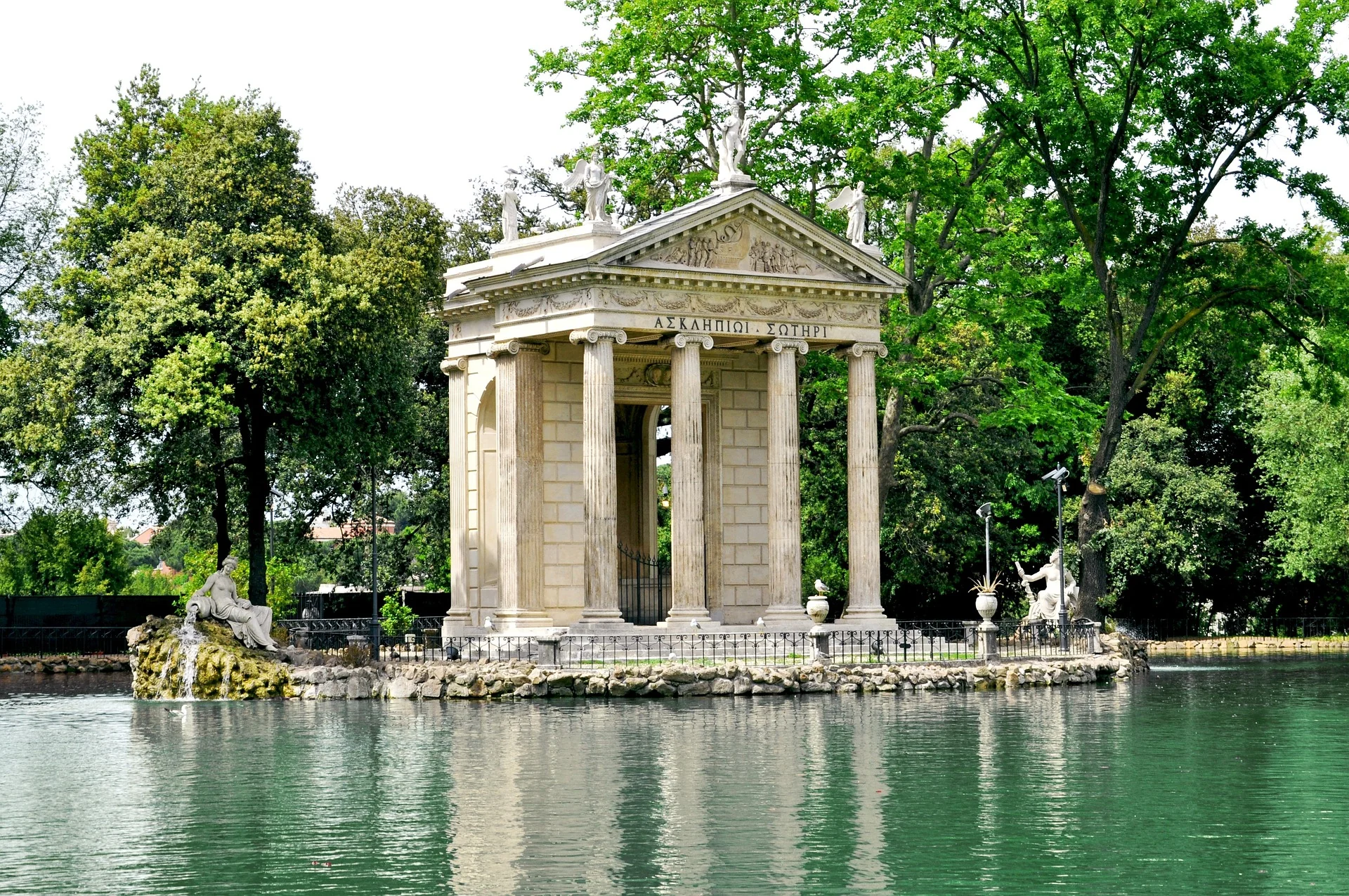 Small neoclassical temple on a lake surrounded by green trees in Villa Borghese