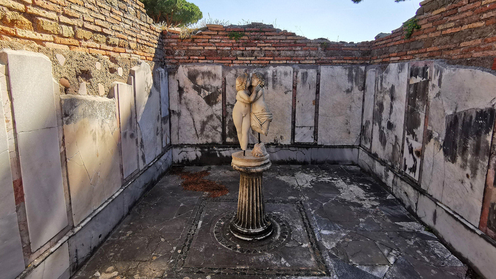 Marble statue of two embracing figures on a column in a ruined niche at Ostia Antica