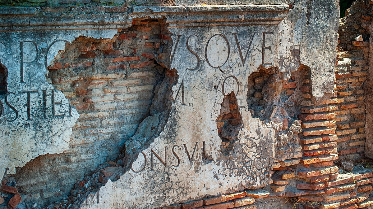 Weathered Latin inscription carved in a crumbling Roman wall
