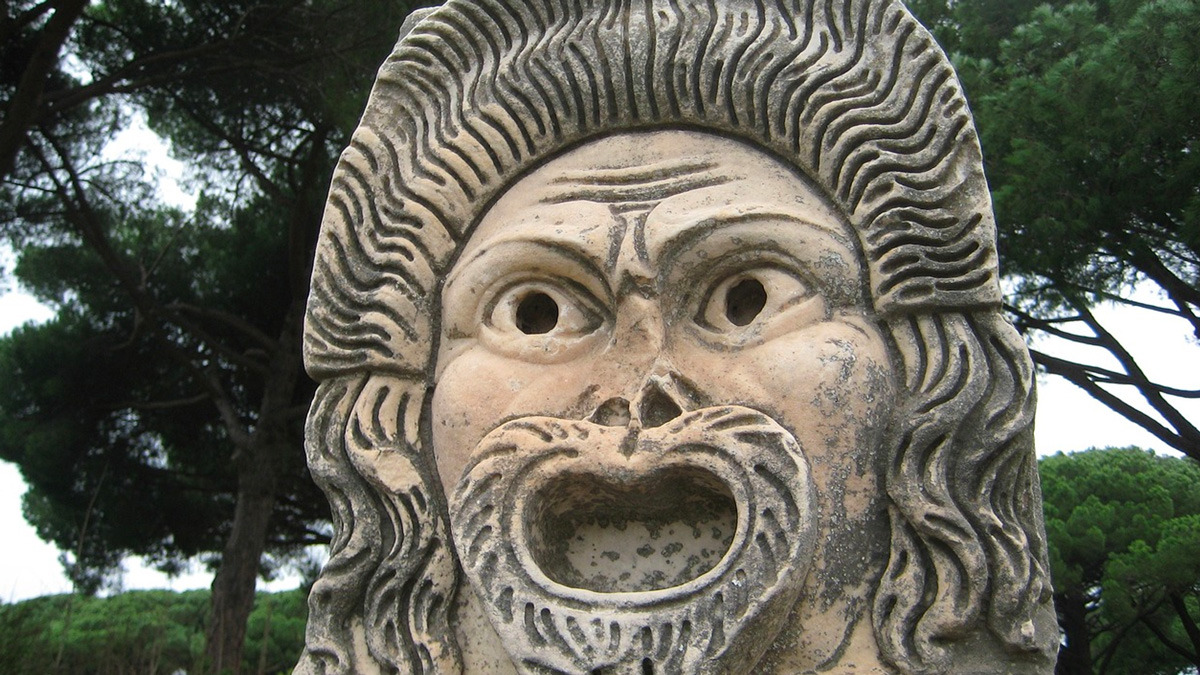 Stone theatre mask with an open mouth set against pine trees at Ostia Antica