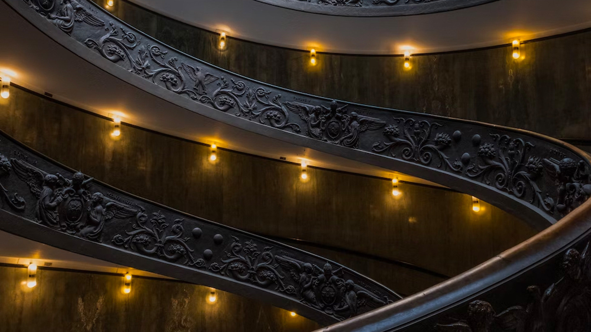 Spiral bronze-railed staircase in the Vatican Museums lit by warm lamps