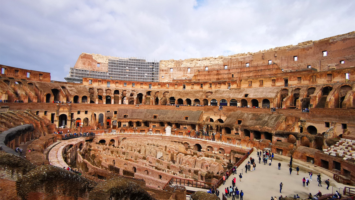 Interior of the Colosseum, showing the arena floor, hypogeum and tiers of arches, with visitors below