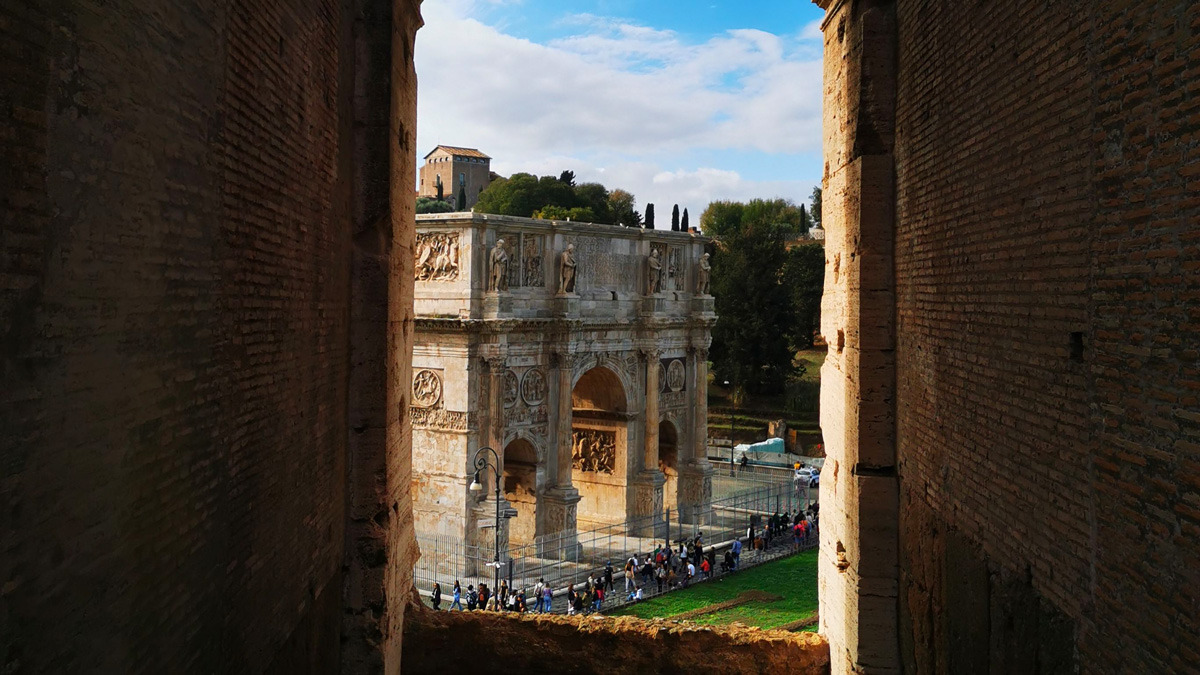 Arch of Constantine seen through a narrow brick opening, with visitors walking in front