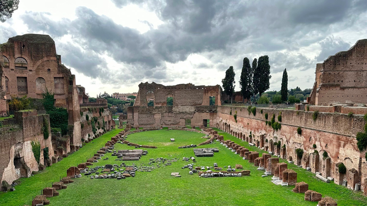 Grassy stadium-shaped garden on the Palatine Hill, ringed by ruined brick walls and cypress trees