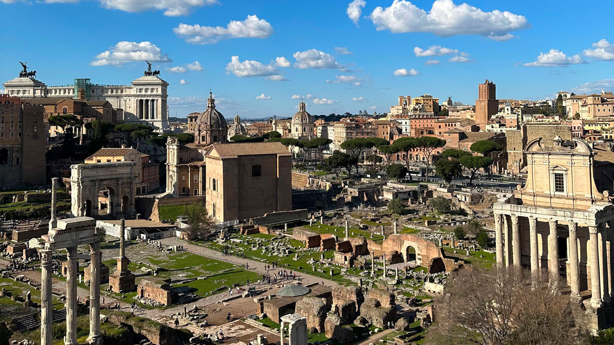 Aerial view of the Roman Forum ruins with columns, arches and the rooftops of Rome beyond