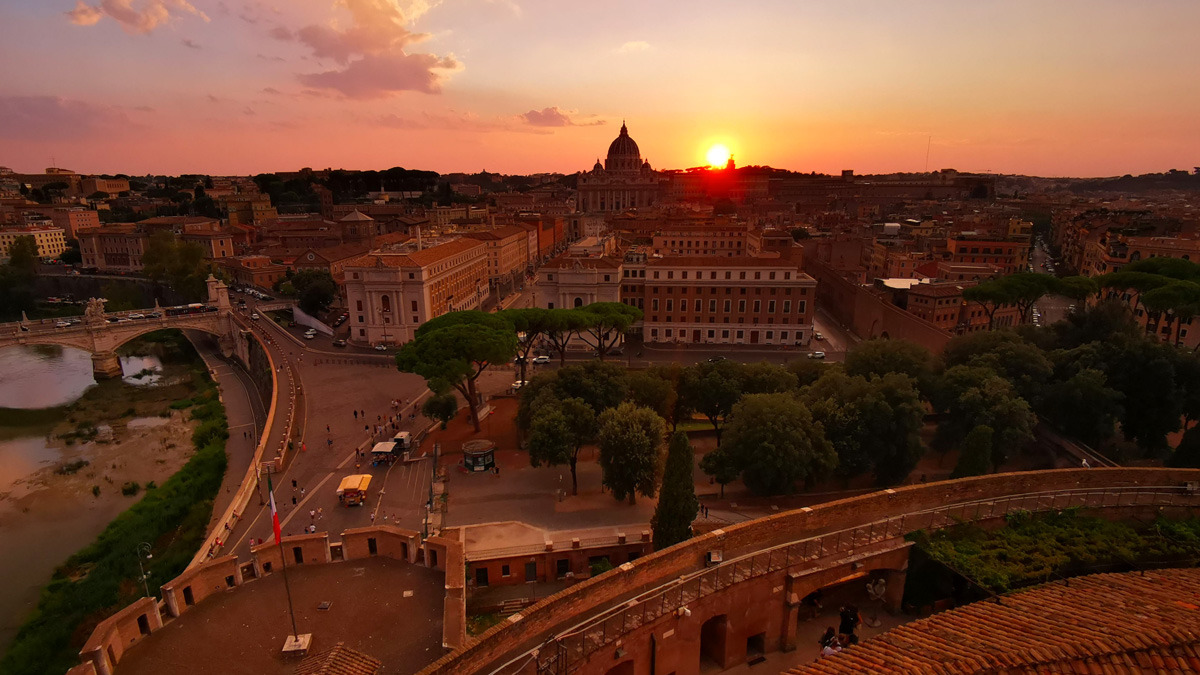 Sunset over Rome seen from above, with the sun setting beside St Peter's dome and the Tiber on the left