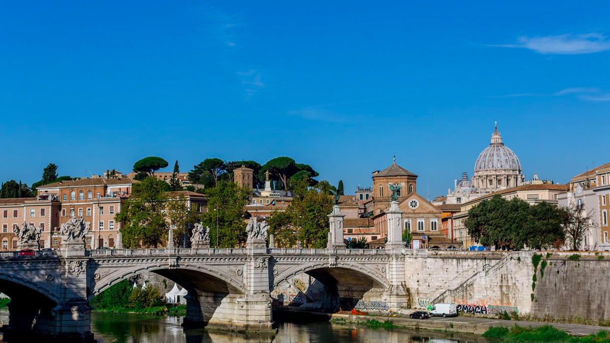Stone bridge with angel statues crossing the Tiber, with St Peter's dome rising behind the rooftops