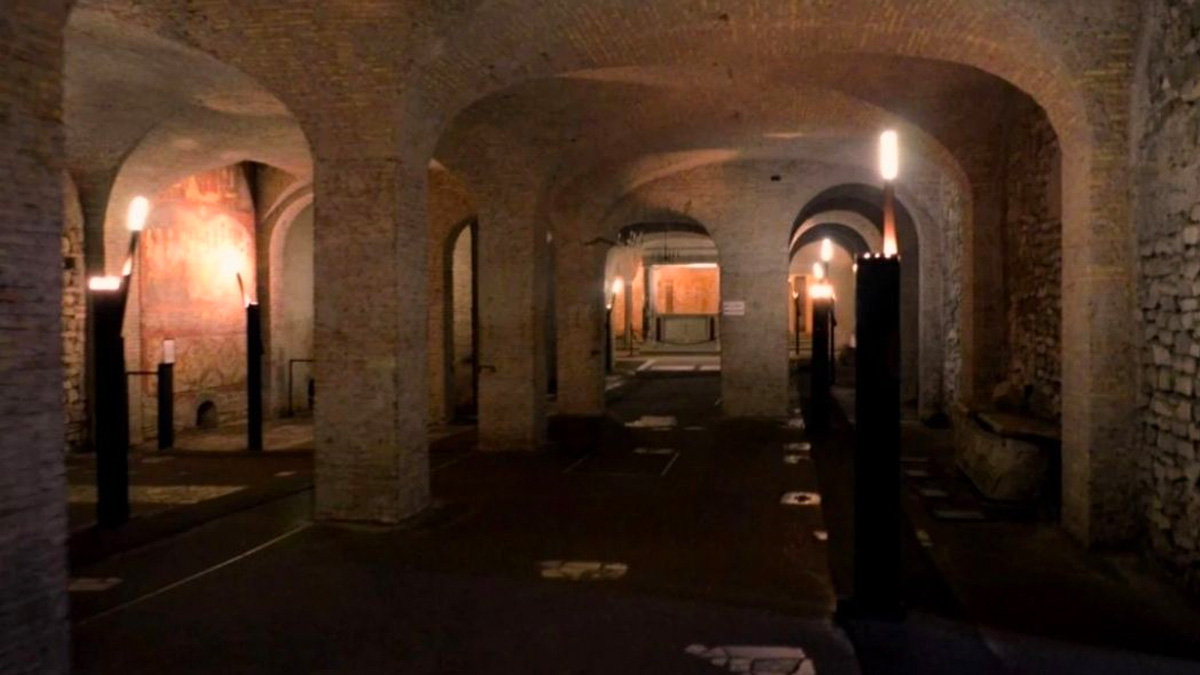 Dimly lit underground vaulted hall with brick arches and tall candle-like lamps