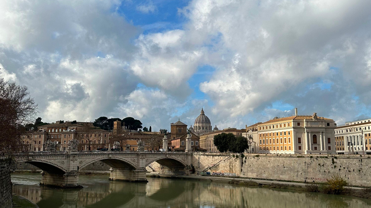 Bridge over the Tiber under a cloudy sky, with St Peter's dome in the distance