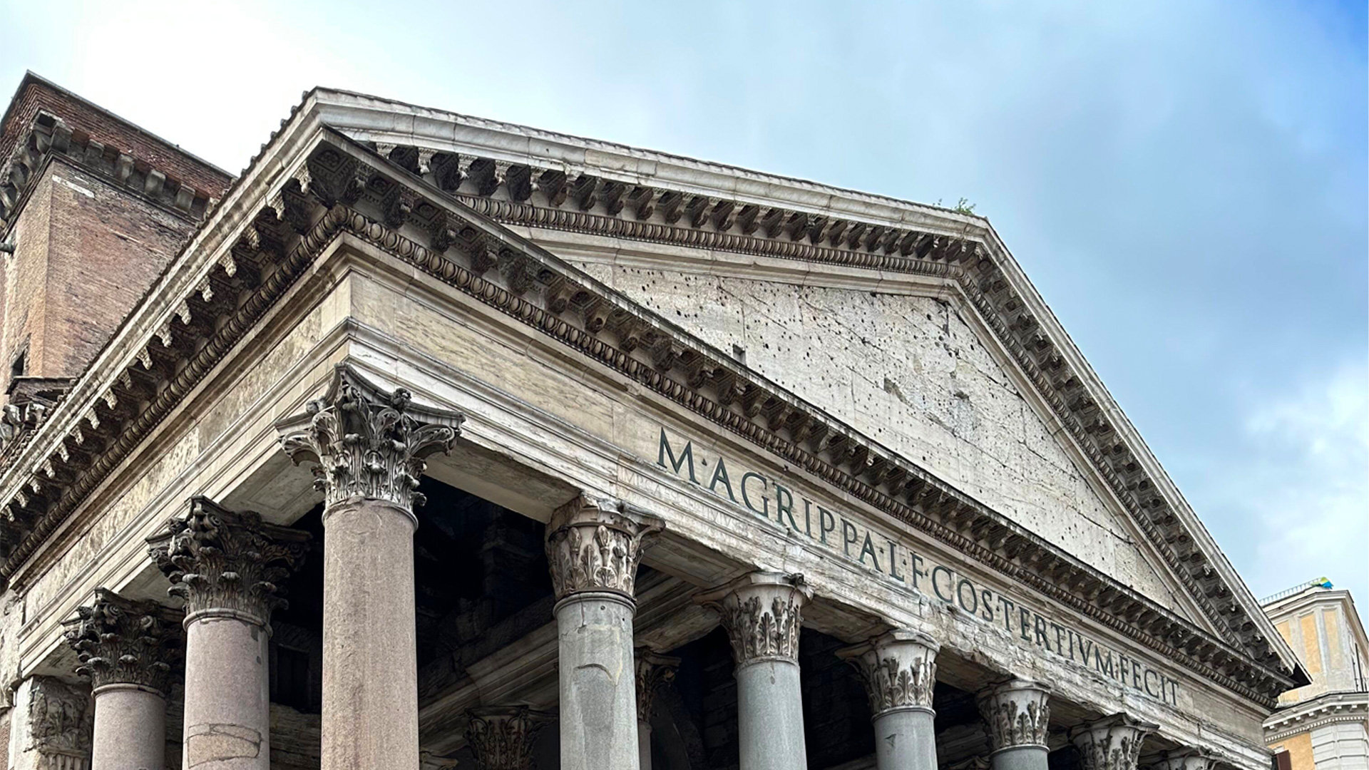 Corinthian columns and pediment of the Pantheon portico under a cloudy sky