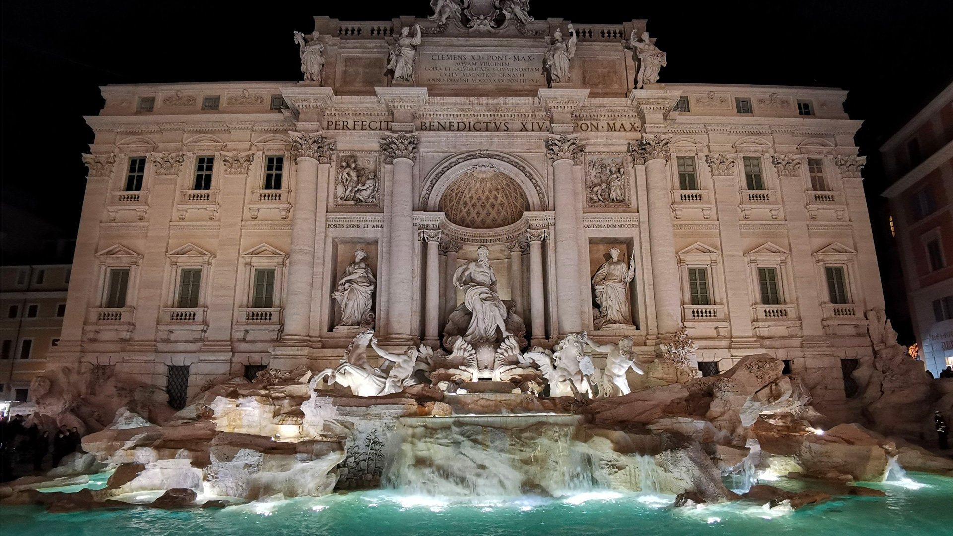 Trevi Fountain lit up at night, its sculpted facade reflected in the turquoise water