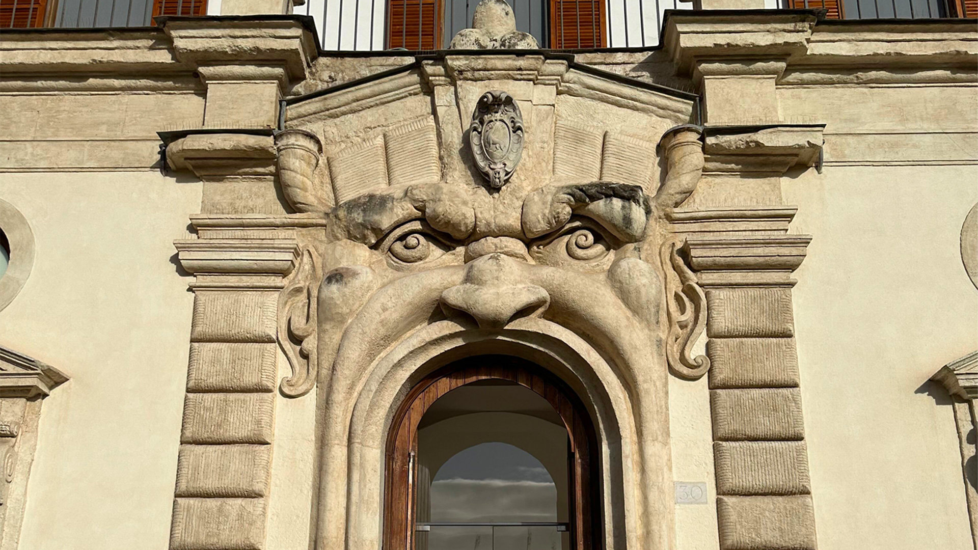 Doorway framed by a carved grotesque face with staring eyes on a Roman palazzo facade