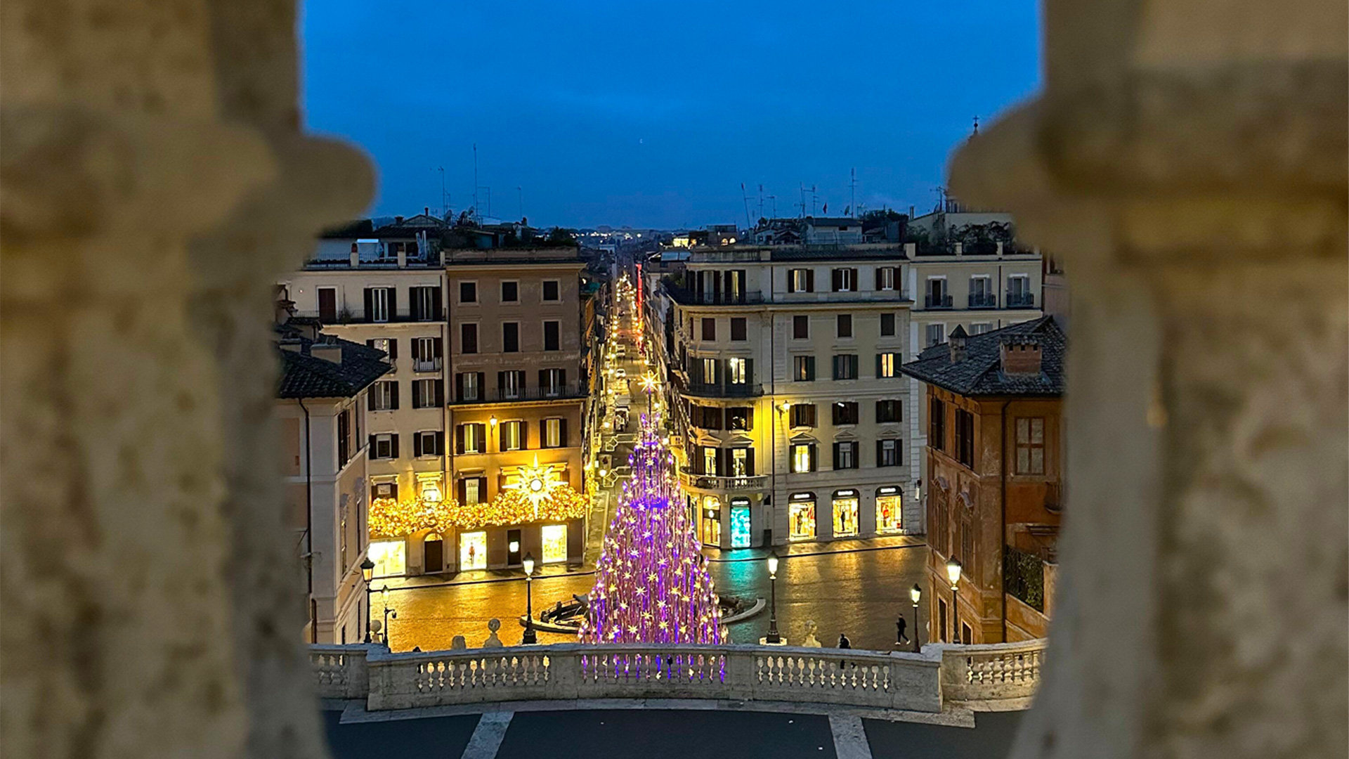 Illuminated Christmas tree at the foot of a street seen through stone balusters at dusk