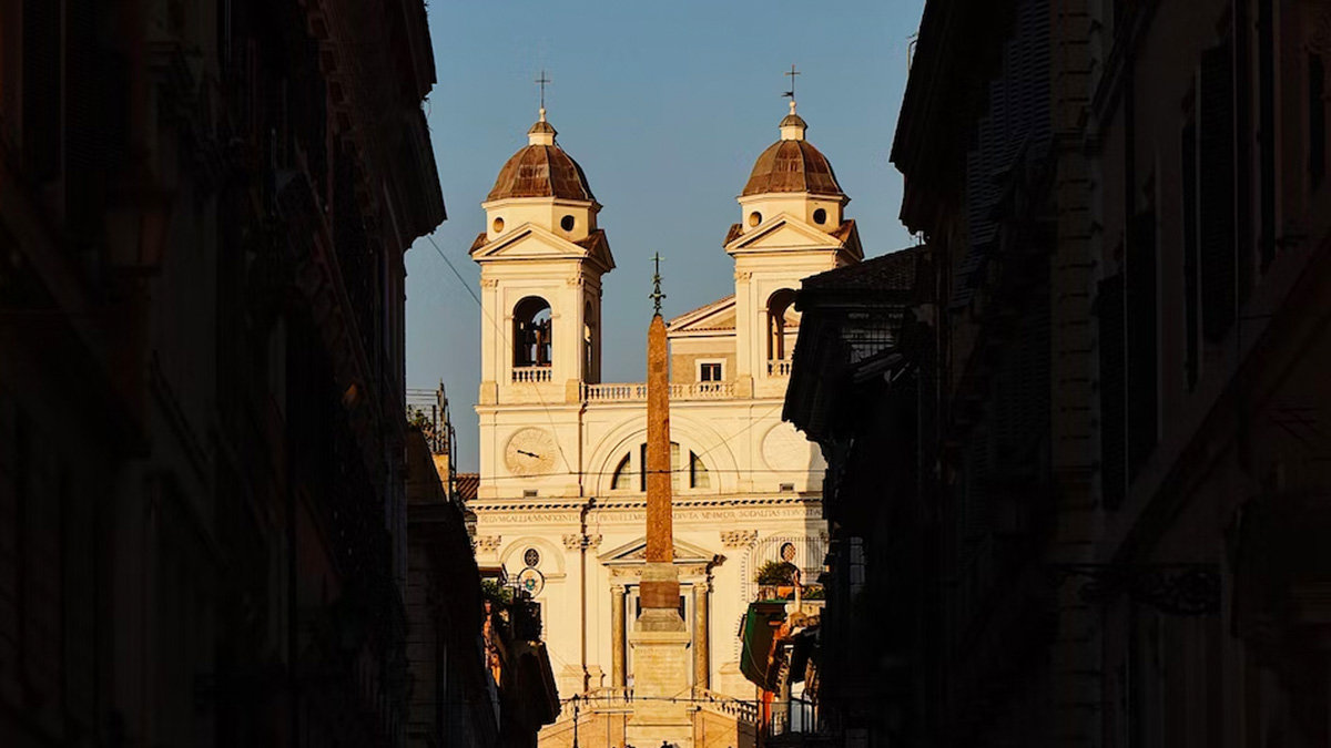 Twin bell towers of Trinità dei Monti glowing in golden light at the end of a shadowed street
