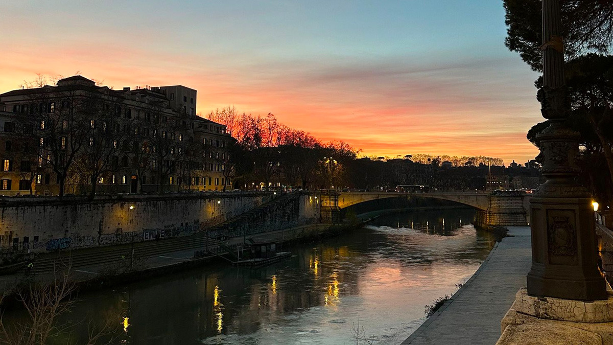 Sunset sky glowing over the Tiber and a stone bridge in Rome