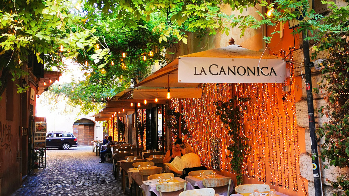 Trattoria terrace in a cobbled Roman lane draped with fairy lights and climbing leaves