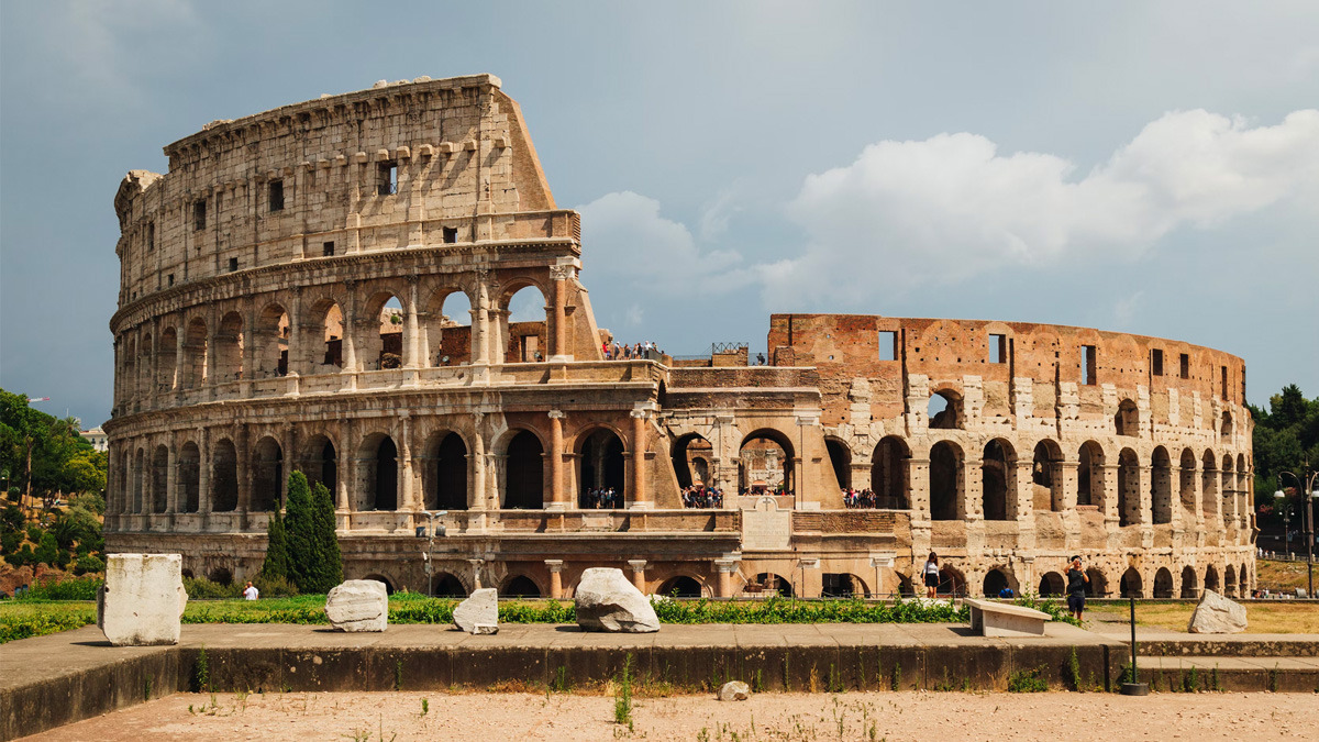 The Colosseum under a cloudy sky with fallen stone blocks in the foreground