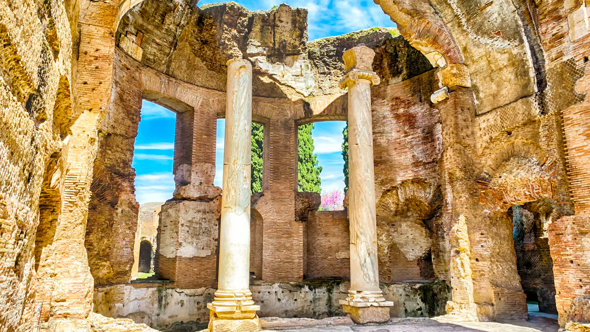 Two marble columns standing among ancient brick walls with sky visible between the arches