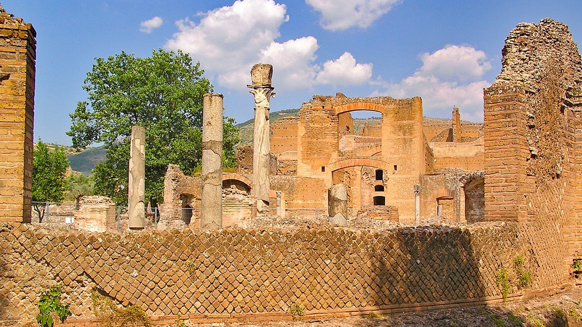 Ancient brick structures and surviving columns rising behind a patterned masonry wall