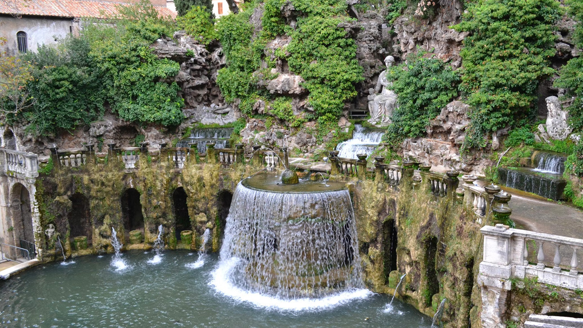 Round fountain spilling water in a garden grotto, covered in moss and greenery